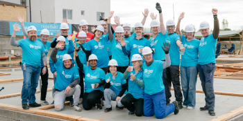 A group of 20 volunteers in matching hard hats and blue Habitat T-shirts pose for a group photo together 