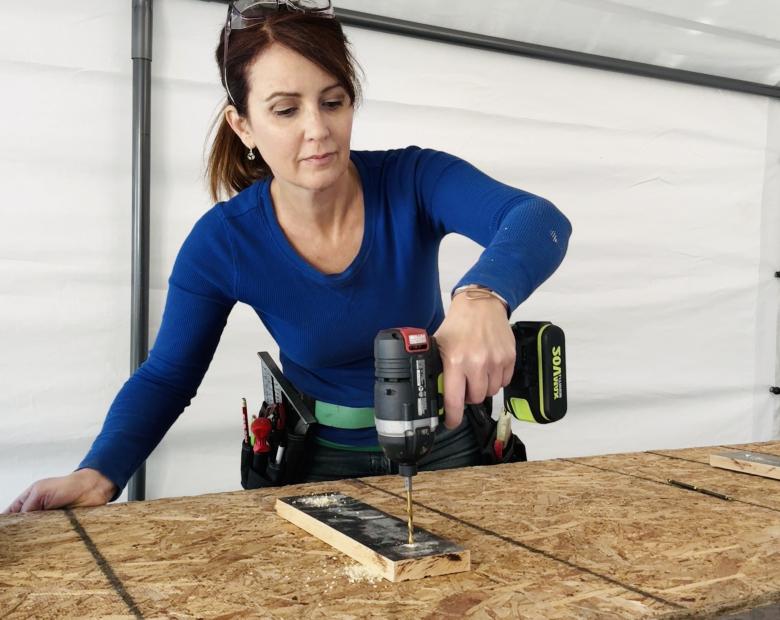 Woman in blue shirt using a drill to attach cleats to a desktop.