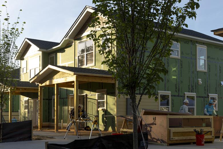 A person in a hardhat is working on a partially completed townhome duplex