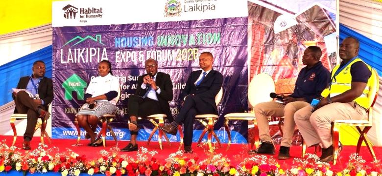 A group of people seated in a panel discussion with a media banner as the backdrop